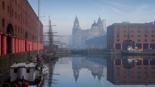 Dock with wooden ship and tall buildings on skyline.