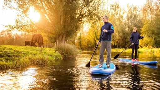 Two people paddleboarding down the River Bure