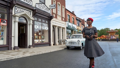 A woman posing in the street in front of shops and cars at a living museum
