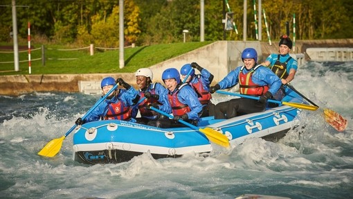 Group of people in a white water raft with paddles on water with rapids