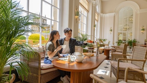 A woman and a man sit by a window and enjoy afternoon tea