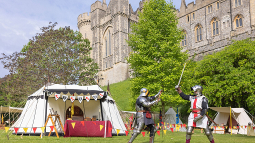 Two men dressed in traditional Armour have a mock sword fight in front of a heritage castle.