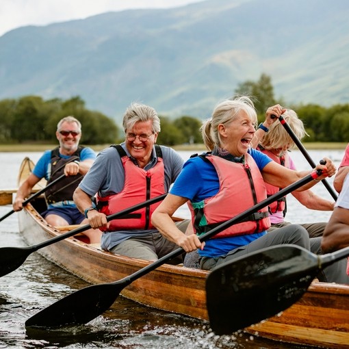 A senior group of friends wearing lifejackets enjoying rowing in a single boat on the River Derwent