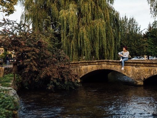 Blond woman wearing hat and jeans sitting on bridge