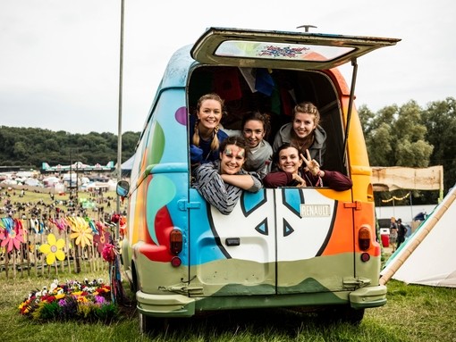 Group of friends smiling out of the back of a rainbow van