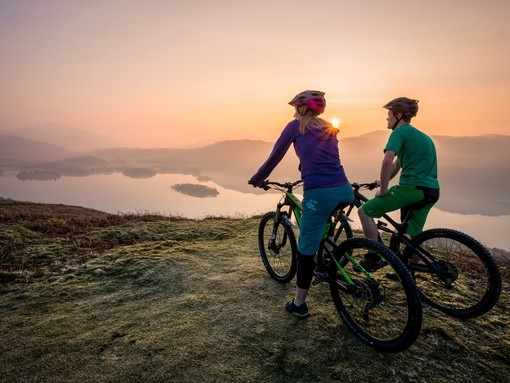 Two people on mountain bikes at the top of a fell at sunset