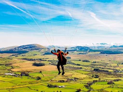 Paraglider gliding over rolling hills and countryside