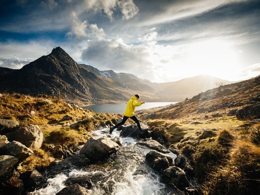A man jumping across a stream whilst hiking