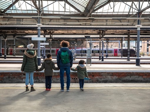 A multiracial family of four, a mother, father and their two little boys standing Newcastle railway station platform waiting for their train.