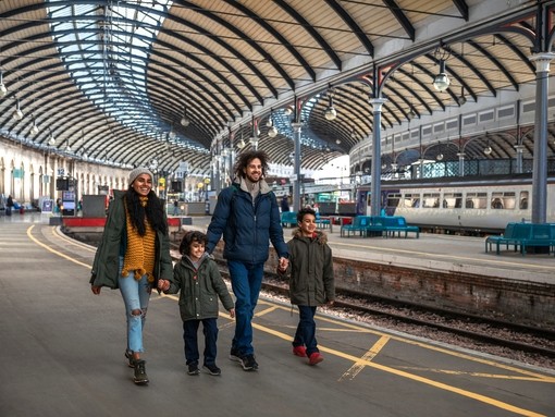 A multi-racial family of four, a mother, father and their two little boys walking along the platform at Newcastle railway station