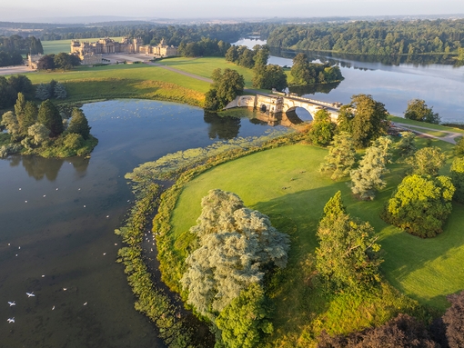 An aerial view of the grounds surrounding Blenheim Palace, an eighteenth-century country house, surrounded by gardens, trees and a lake crossed by a bridge to reach the front of the house. Blenheim Palace - Silver award winner for the Large Visitor Attraction of the Year at the VisitEngland Awards for Excellence 2023.