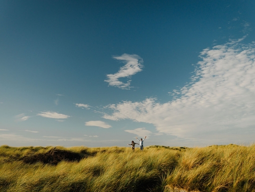 Two young young boys jump in sand dunes at a beach