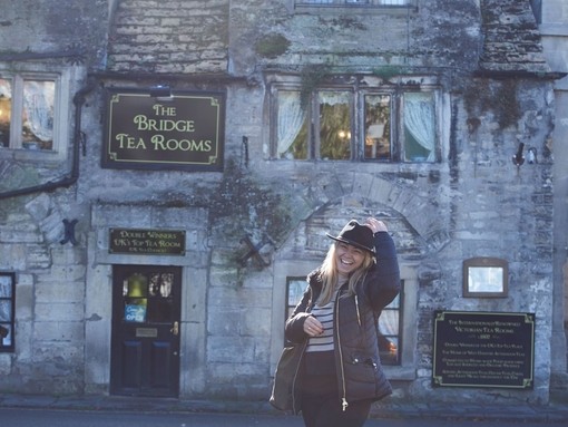 Smiling woman standing outside and old style cafe holding on to a black hat.