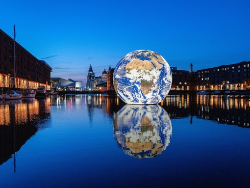 A sphere earth artwork floating in the middle of the docks surrounded by buildings and lit up at night