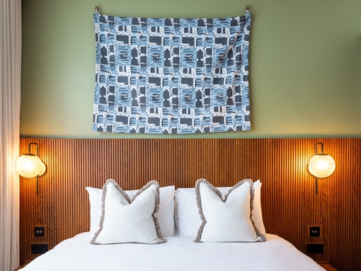 A hotel room bed with crisp white sheets and pillows with a wooden headboard against a green wall