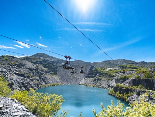 People on a high zip wire going over a quarry filled with water.