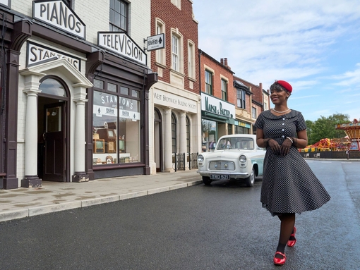 A woman posing in the street in front of shops and cars at a living museum