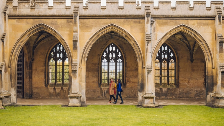 Two women walking under the arches of a college quad