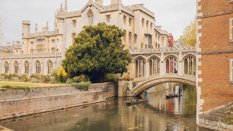 People punting on the river under a bridge in front of an historical building