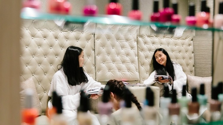 Two women, sat in white robes, getting their nails done
