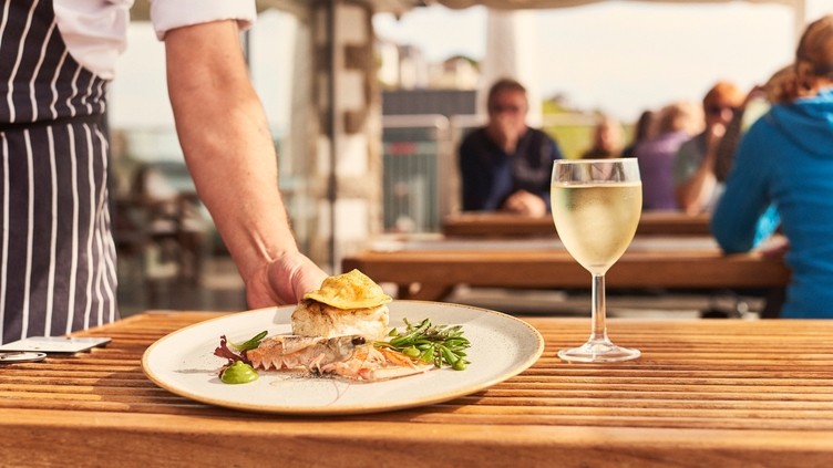 Waiter placing plate of food on table beside glass of wine