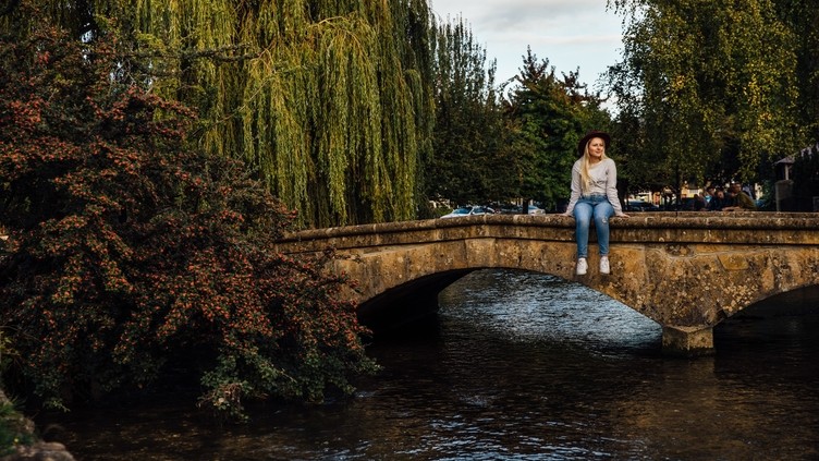 Blond woman wearing hat and jeans sitting on bridge