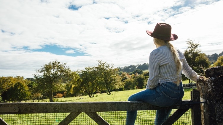 Woman sitting on wooden gate looking at greenery