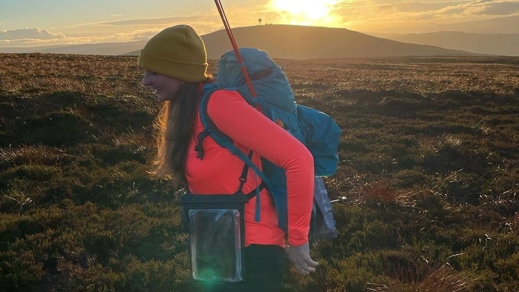 Female hiker with a backpack and walking poles, hiking through the countryside of Kielder in Northumberland at sunrise