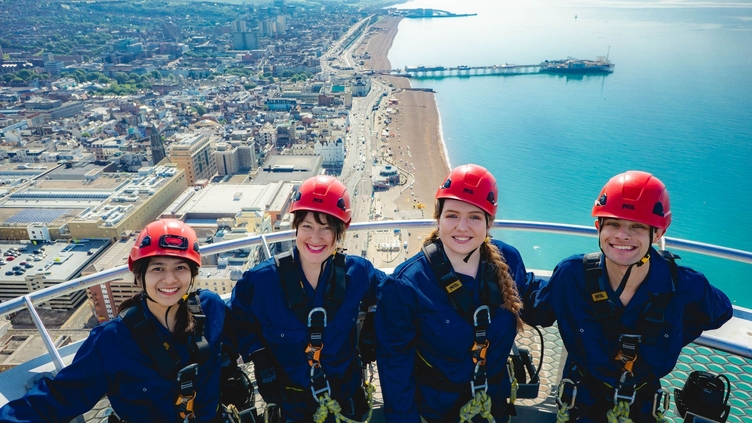Group of friends in climbing gear at the top of a panoramic tower with coastline on the background