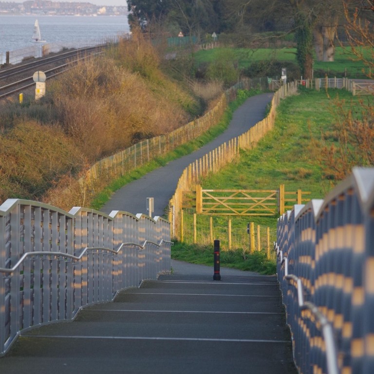 View down a bridge over a train line with the estuary in the distance