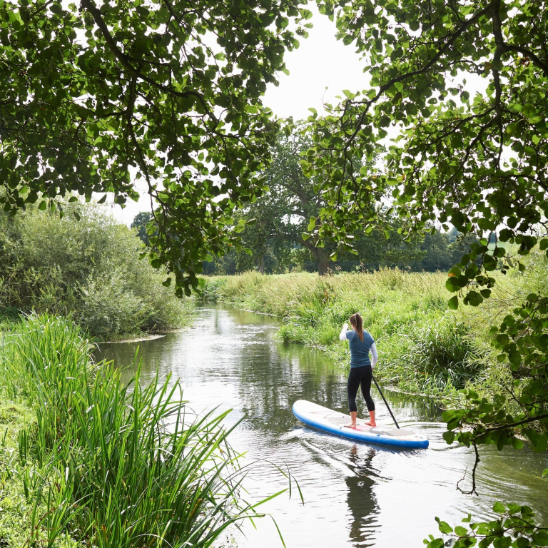 Young woman paddle boarding on River Wensum, in the Wensum Valley, Norfolk