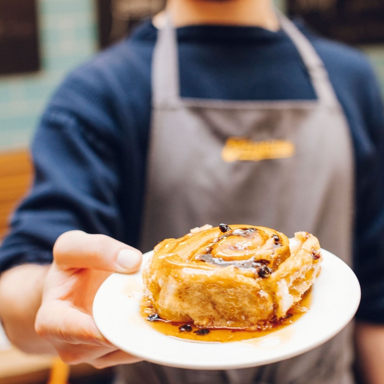 Man holding a pastry on a plate outside restaurant