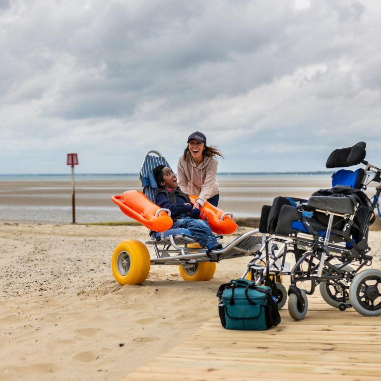 A woman laughs with her son who sits in an accessible sea wheelchair