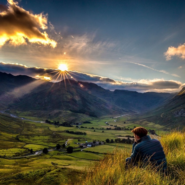 Man sitting in long grass watching sunrise between valleys