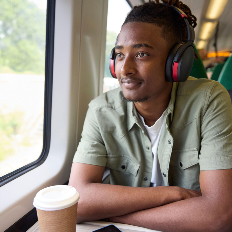 A young man sitting on a train with wireless headphones