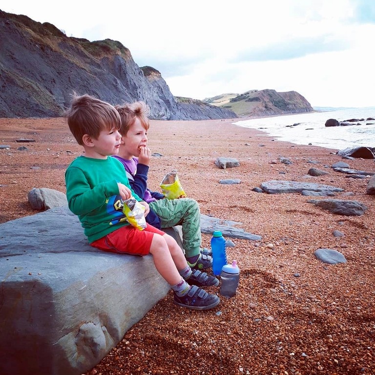 Two boys sitting on a rock and eating crisps on a beach