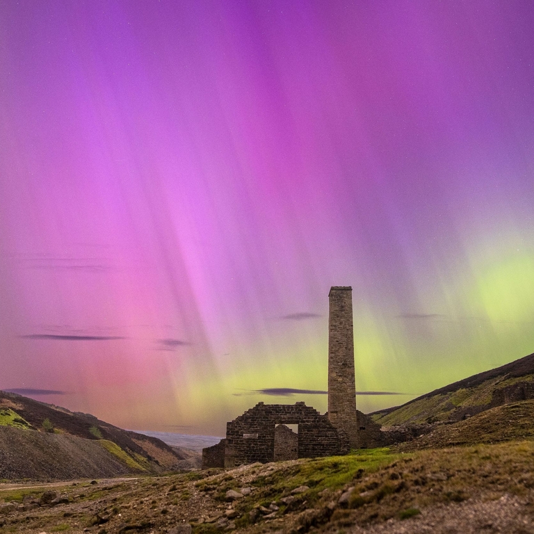 The aurora borealis in the remote countryside by stone house ruins.