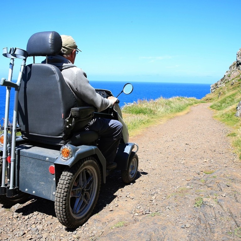 Senior man riding a tramper on a pebbly path on the coast