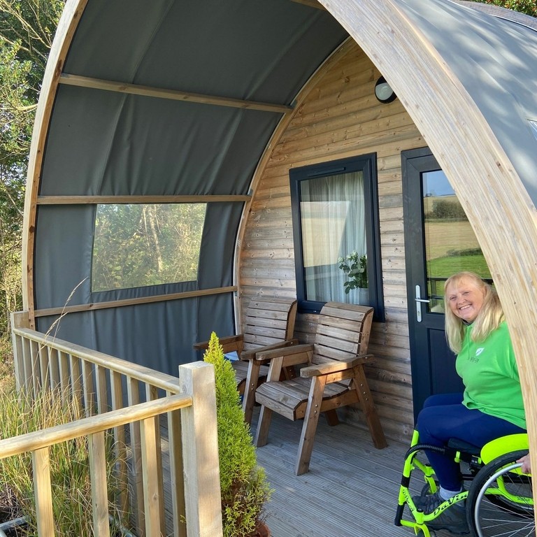 Woman sitting in a wheelchair cycle outside wooden hut