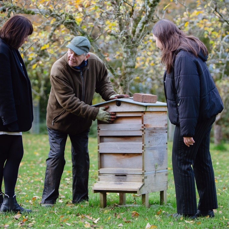 Three people looking at beehive in a garden