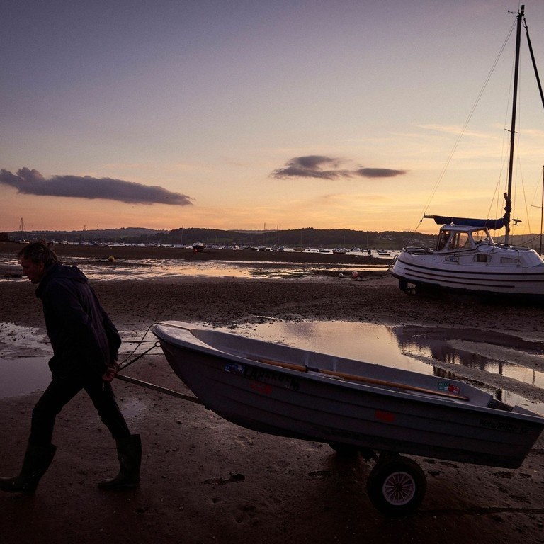 Silhouette of man pulling small rowboat along beach
