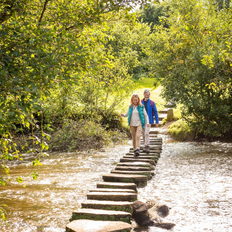 Couple stepping across some stepping stones across a river