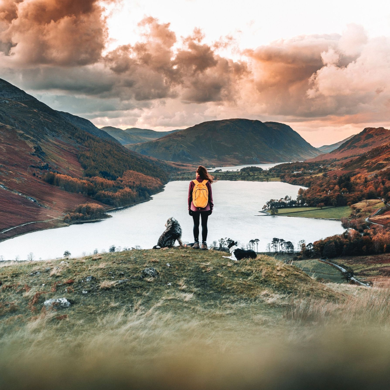 Woman standing with two dogs looking down at a lake in a valley