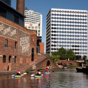 Group of people paddleboarding past industrial buildings on a canal