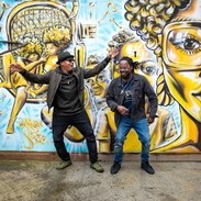 Two men standing in front of street art, dancing