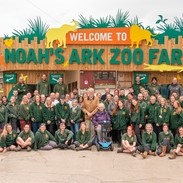A sign which reads "Welcome to Noah's Ark Zoo Farm" with various staff members standing in front wearing matching branded tops. Noahs Ark Zoo Farm - Gold award winner for the Accessible and Inclusive Tourism Award at the VisitEngland Awards for Excellence 2023.