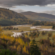 Landscape shot of a countryside view with a mountain backdrop and a stream running through the centre. 