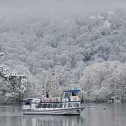 A boat cruising on a lake in winter, snow covering the surrounding woods