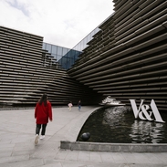 A woman and two girls walking by a modern museum.