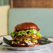 A burger stacked with meat, cheese, pickles and lettuce on a plate, on a marble table.